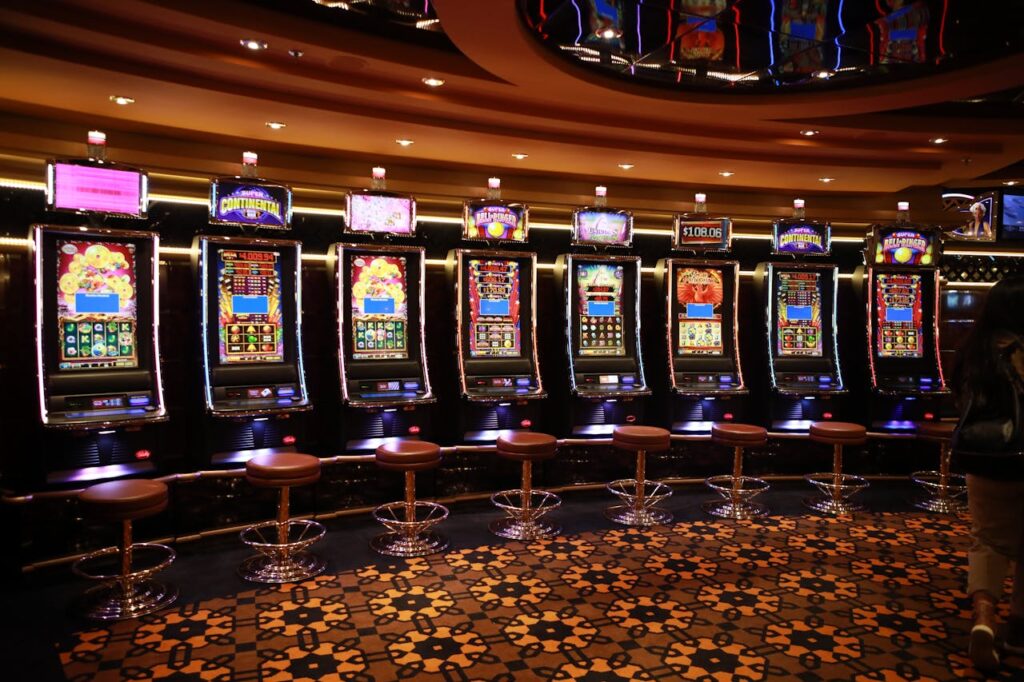 Dubibet Access Page | Quick Login & New User Register. A row of luxury slot machines in a casino interior with plush stools, perfect for gaming enthusiasts.