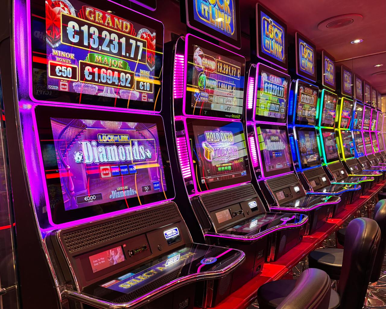 Dubibet Colorful slot machines lined up in a casino with neon lights and jackpot displays.