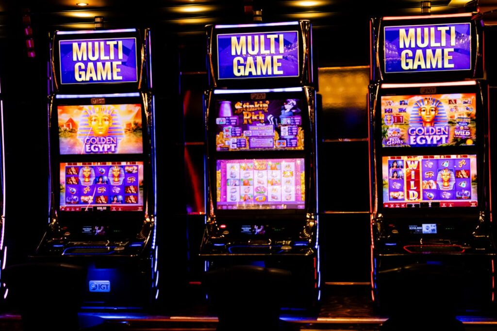 Dubibet Entry Gate Three illuminated slot machines in a bustling casino at night.