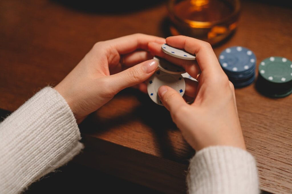 Dubibet Official Access | Login to Casino & Sportsbook A person in a white sweater playing with poker chips on a wooden table.
